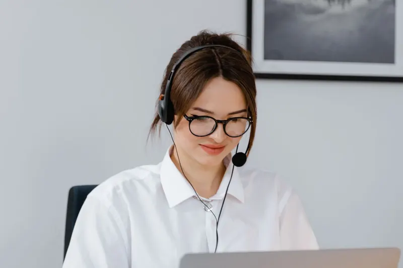 Atendente de camisa branca e óculos usando headset diante de um notebook